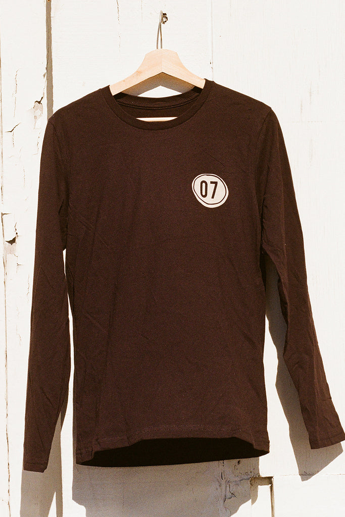 Black 07 long-sleeve shirt with a circular logo on a hanger against a white wall.