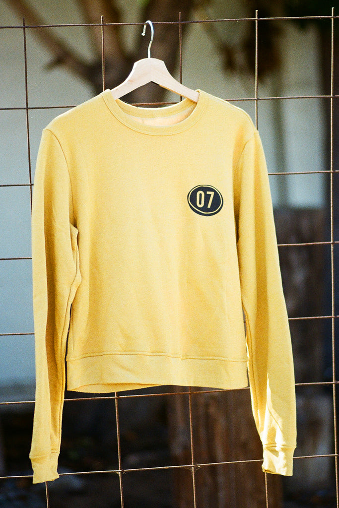 Yellow sweatshirt with a black circle and number '07' on a hanger against a tiled wall.