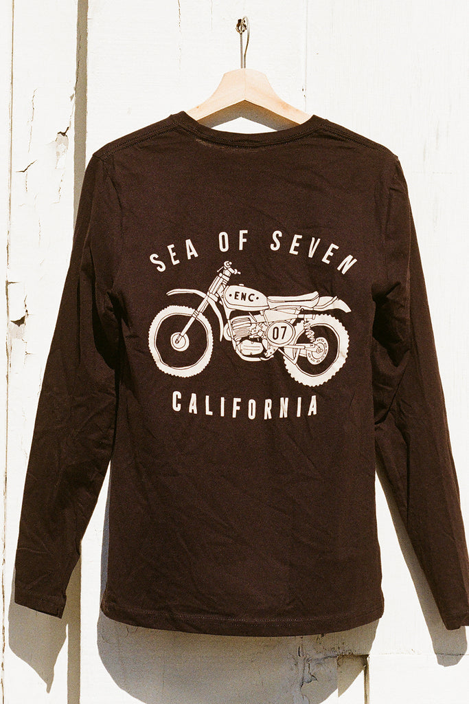 Black long-sleeve shirt with motorcycle graphic and text 'SEA OF SEVEN ENC 07 CALIFORNIA' on a hanger against a white wall.