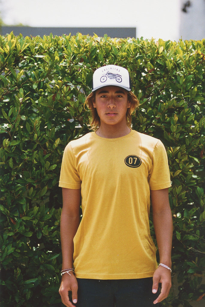 men wearing a white trucker hat with a motocross dirt bike and a mustard yellow short sleeve tee with the number 07