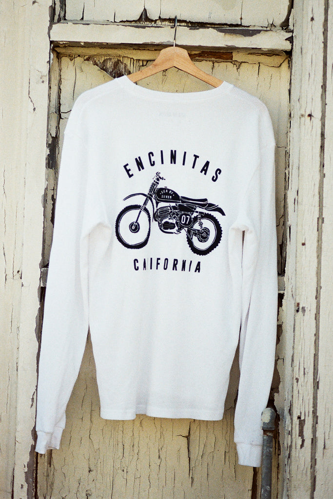 White long-sleeve shirt with a motorcycle graphic and 'Encinitas California' text on a wooden door background