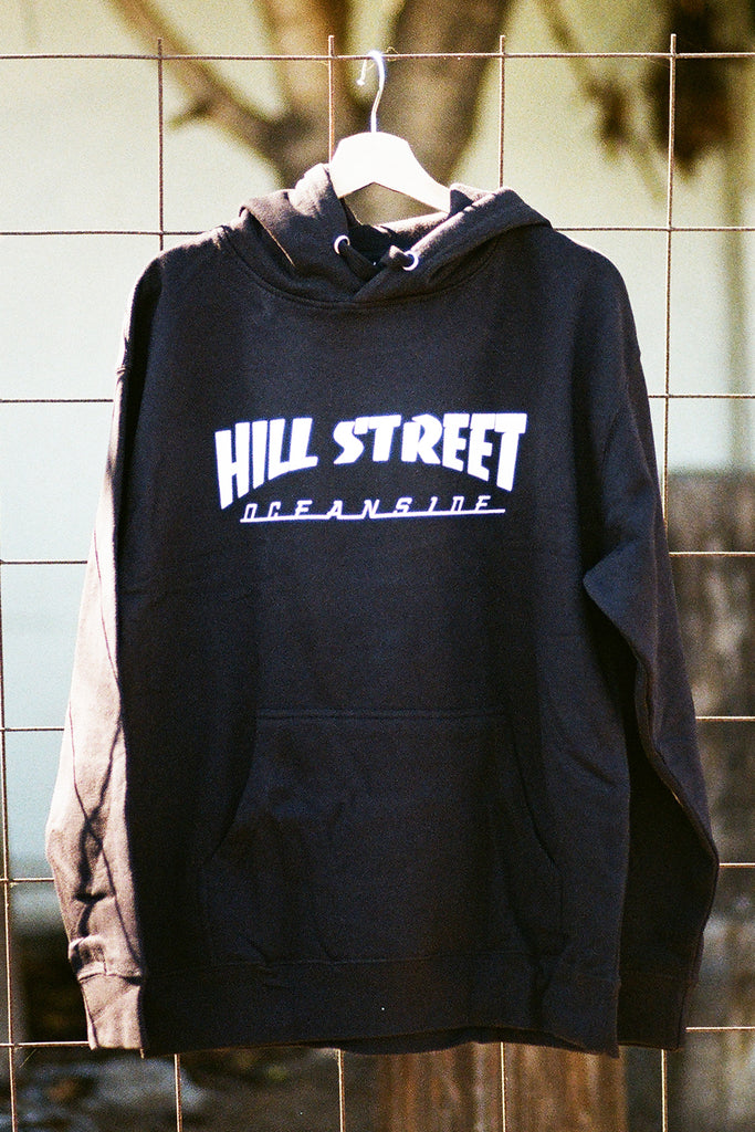 Black hoodie with 'Hill Street' text on a hanger against a tiled wall.