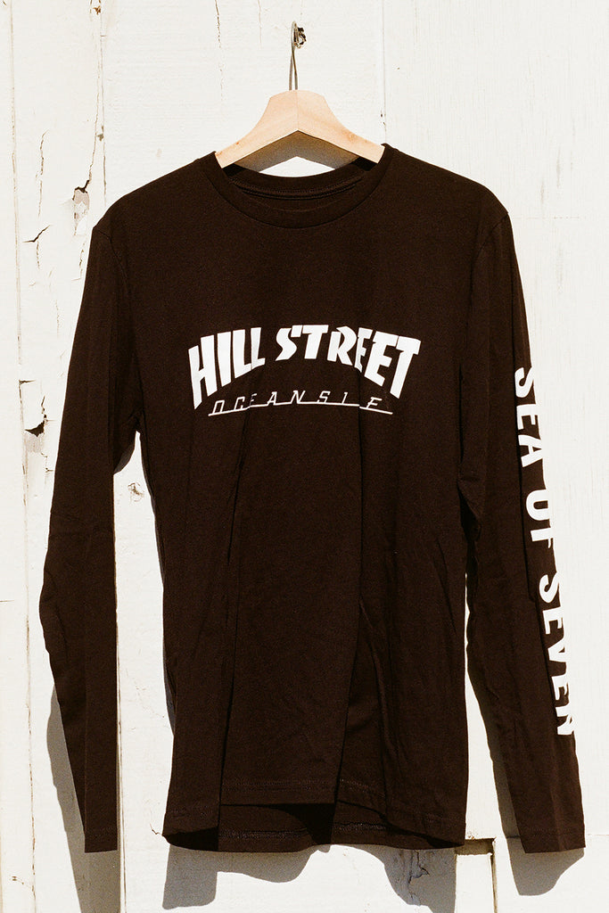 Black long-sleeve shirt with 'Hill Street' text on a wooden hanger against a white wall.