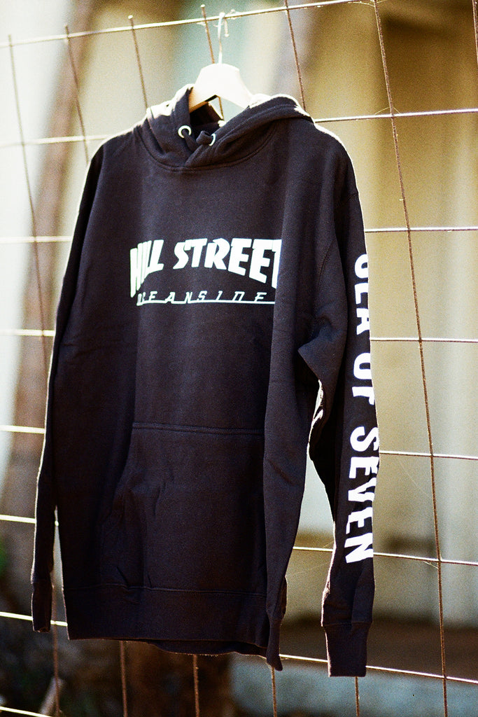 Black hoodie with white text 'HILL STREET OCEANSIDE' on a hanger against a wire mesh background