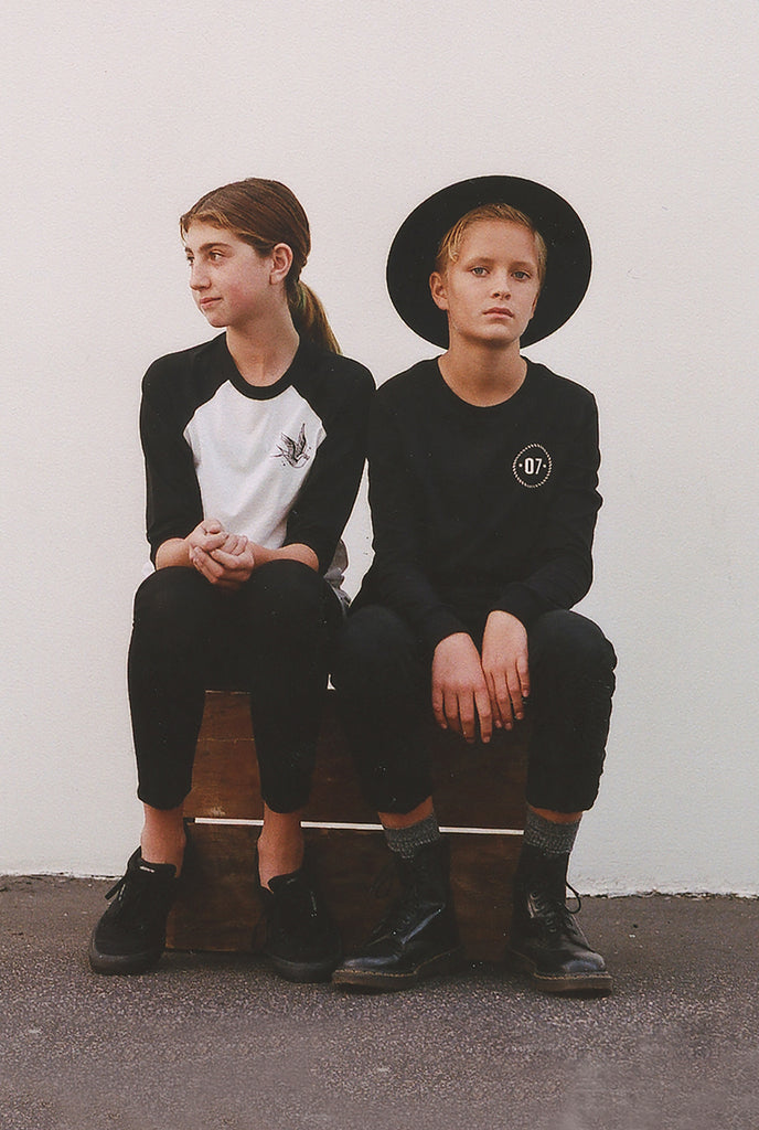 modern looking boy and girl sitting next to each other with a white wall on a brown box.