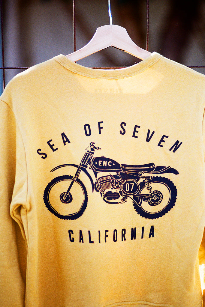 Yellow sweatshirt with a motorcycle graphic and text 'SEA OF SEVEN ENC 07 CALIFORNIA' on a hanger