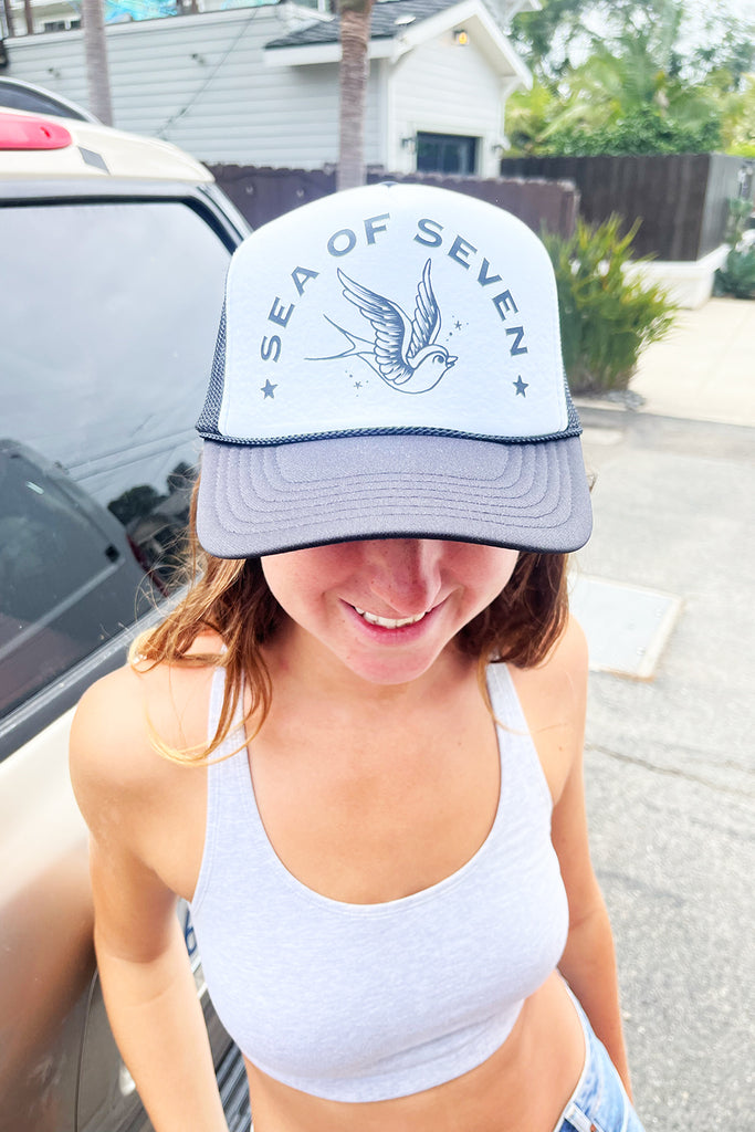 Person wearing a sea of seven trucker hat with a swallow bird outside
