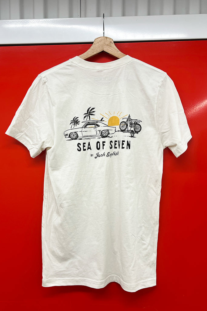 White t-shirt with graphic design of a vintage muscle car with a surfboard towing a vintage motocross dirt bike and text that says sea of seven by jack english.