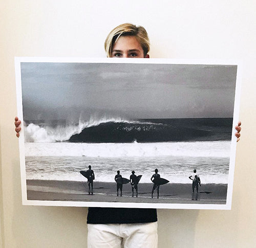 Gavin Mestler holding a surfing posters titled Standing Room Only of a group of surfers on the shoreline at surf spot Pipeline on the North Shore of Oahu in Hawaii.
